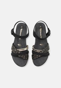 Mustat sandaalit, joissa on punottuja mustia ja kultaisia nauhoja, solkisäädettävä hihna ja tasainen kumipohja. Kengän pohjassa koko 37.