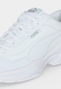 Gros plan d'une basket blanche Puma avec lacets, avec le logo Puma sur le côté et la languette, et une semelle épaisse et rembourrée.