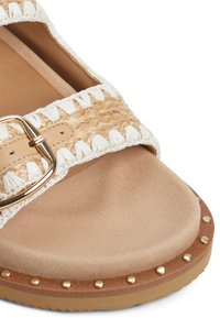 Woven beige and white slide sandal with a tan fabric footbed and gold hardware. Features a cushioned sole and metallic studs around the edge.
