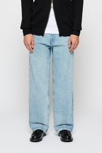 Persoon in lichtblauwe wijdvallende jeans, zwarte leren tassellaarzen, een wit shirt en een zwarte zip-up trui.
