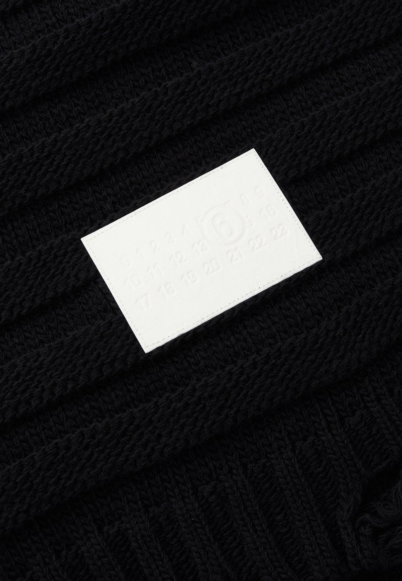 Svart stickad tyg med strukturerade ränder; har en vit rektangulär etikett präglad med siffror och en cirkulär logotyp.