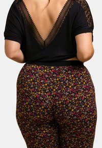 Haut noir avec bordure en dentelle et dos en V profond, associé à un pantalon noir avec un motif floral coloré en jaune, rose et violet.