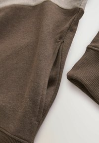 Dark brown sweatshirt made of soft fabric, featuring a light gray shoulder panel and ribbed cuffs. Includes side pockets for added functionality.