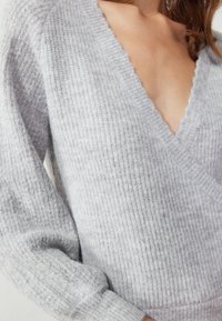 Light grey knitted sweater with a deep V-neck, textured ribbing, and long sleeves featuring a slightly oversized fit.