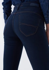 Mørkeblå jeans lavet af denim, med kontrastsyning, tætsiddende ben og en høj talje med et særligt design på baglommen.
