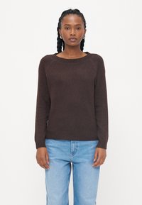 Brun strikket genser med rund hals og lange ermer, kombinert med lys blå denimjeans. Glatt tekstur, ingen synlige mønstre.