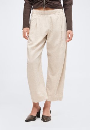 Beżowe szerokie spodnie z elastycznym pasem noszone z czarnymi butami na słupku z ostrym noskiem oraz krótkim brązowym topem.