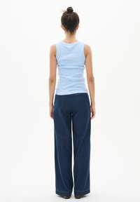 Heleheline ribadega tank top, mis on kombineeritud laia jalgadega tumedast denimpükstest. Kangas tundub pehme, laia lõike ja sirge jala siluettiga.