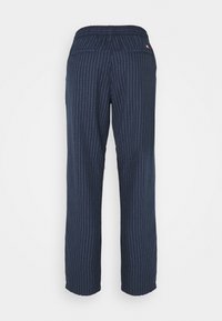 Granatowe spodnie z pionowymi białymi paskami, wyposażone w elastyczny pas i dwie tylne kieszenie, wykonane z teksturowanej tkaniny.