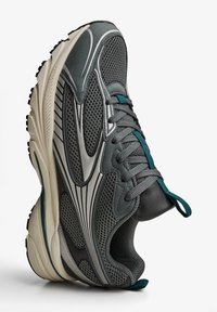 Grå atletiska skor med övre del i mesh och silverdetaljer, texturerad sula och accenter i teal på snörningen. Lättviktsdesign med vaddering.