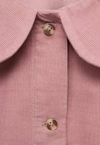 Tessuto in velluto a coste rosa con una trama a coste, caratterizzato da un colletto arrotondato e una chiusura con un singolo bottone beige al collo.