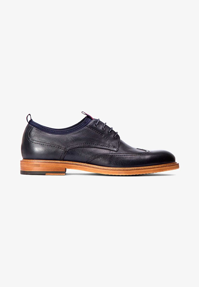 Zwarte leren dress shoe met een ronde neus, decoratieve stiksels en vijf oogjes. Heeft een bruine houten zool en een marineblauw accent bij de kraag.