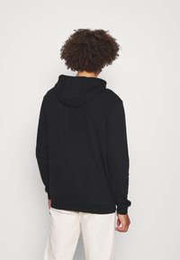Sudadera con capucha negra de corte relajado, con puños y dobladillo acanalados, y textura suave. Presenta un diseño simple sin logotipos ni patrones visibles.