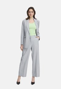 Blazer gris clair et pantalon large associés à un débardeur ajusté vert lime. Tissu lisse avec une couture classique. Escarpins noirs à bout pointu.