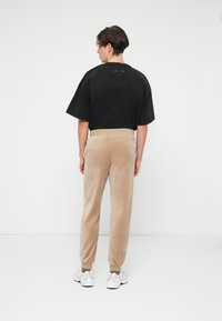 Camiseta negra de gran tamaño con mangas cortas, combinada con joggers de terciopelo beige claro que presentan una cinturilla acanalada y bolsillos laterales.