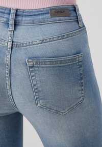 Jeans de denim azul claro con un diseño clásico de cinco bolsillos, costuras visibles y una pequeña etiqueta en la cintura.