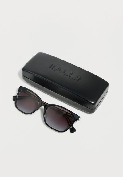 Μαύρα γυαλιά ηλίου Ralph Lauren με βαθμιαία σκουραμένοι φακοί δίπλα σε μαύρη θήκη που φέρει ανάγλυφο το λογότυπο "Ralph Lauren" σε λευκό φόντο.