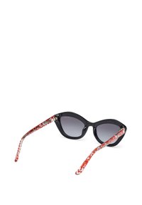 Gafas de sol de ojo de gato con montura negra y lentes degradados; brazos rojos estampados y transparentes. La silueta tiene ángulos agudos y un acabado brillante.