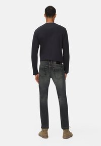 Pull bleu foncé, jean gris ajusté avec des accents décolorés, et bottes beiges. Texture lisse, design décontracté, détails de couture subtils sur le jean.