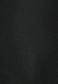 Gros plan d’un tissu noir montrant un motif texturé fin et étroitement tissé avec de subtiles lignes diagonales.