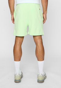 Lys grønne sports shorts med elastisk talje, sidelommer og en enkel kant. B�året med hvide ankelsokker og grå løbesko.
