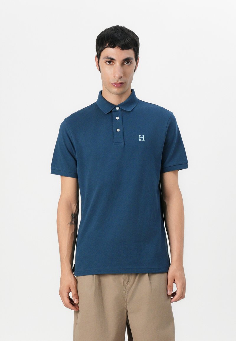 Ναυτική πόλο μπλούζα με σχεδιασμό για καλοκαιρινά, τρία κουμπιά και κεντητό λογότυπο στην αριστερή πλευρά. Κοντά μανίκια, λεία υφή και κλασική γραμμή.