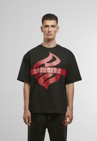 Juoda per didelė T-marškinė su dideliu raudonų liepsnų grafiku ir baltu "ROCAWEAR" tekstu. Medvilninė medžiaga, trumpomis rankovėmis ir apvaliu iškirpimu.