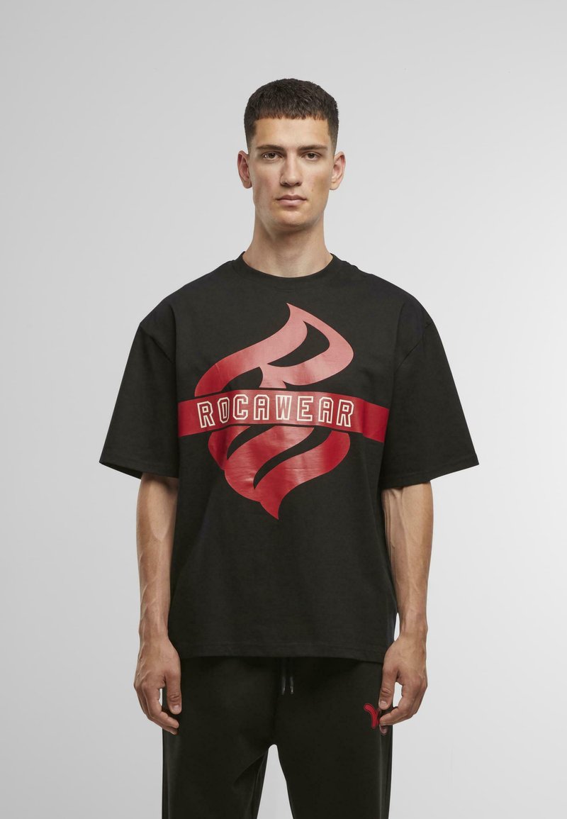 Juoda per didelė T-marškinė su dideliu raudonų liepsnų grafiku ir baltu "ROCAWEAR" tekstu. Medvilninė medžiaga, trumpomis rankovėmis ir apvaliu iškirpimu.