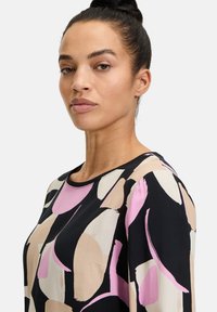 Bunt gemustertes Oberteil mit auffälligen abstrakten Mustern in Pink, Beige und Schwarz. Glatte Stoffqualität mit rundem Ausschnitt und lässiger Passform.