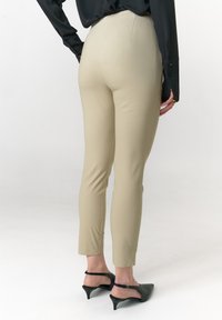 Beige Slim-Fit-Hosen aus Stretchstoff mit glatter Textur, mit mittelhohem Bund und verkürzter Länge, kombiniert mit schwarzen Sandalen mit Absatz.