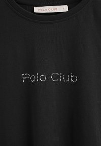 Camiseta de algodón negra con cuello redondo, que presenta "Polo Club" en pedrería en el pecho. Textura suave, corte estándar.