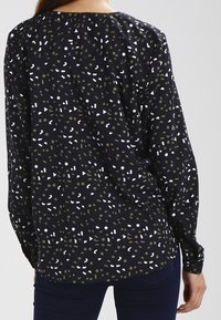 Blusa nera con maniche lunghe, caratterizzata da un motivo di forme verdi, bianche e beige. Tessuto liscio con scollatura rotonda e polsini con bottoni.