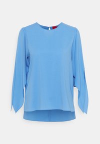 Top blu chiaro realizzato in tessuto morbido, con scollatura rotonda, maniche lunghe con fessure e un'apertura a chiave sul retro.