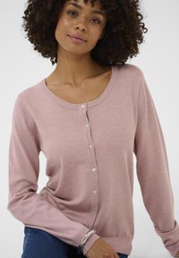 Hellrosa Strickjacke mit rundem Ausschnitt, gerippten Kanten und sieben Knöpfen vorne. Weiche Textur und lange Ärmel.