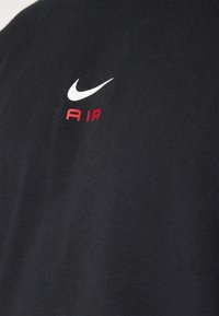 Black fabric with a small white Nike swoosh logo above red "AIR" text on clothing, showing texture and stitching details.