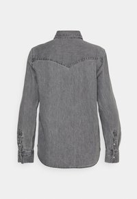 Chemise en denim gris à manches longues, col pointu et poignets à boutons. Présente un empiècement au dos et un ourlet arrondi.