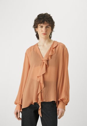 Peach-colored blouse with a V-neck, ruffled front, and long sleeves. Made of lightweight fabric, featuring button closure and a flowing hem.