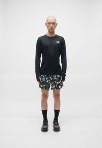 Svart langermet skjorte, shorts med blomstermønster, svarte sokker og svarte sko. Skjorten har en logo; shortsen har livlige flerfargede blomster.