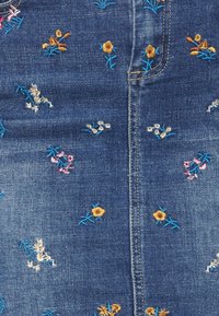 Tissu denim bleu avec de petits motifs floraux brodés en jaune, blanc et rose dispersés, présentant une couture piquée.