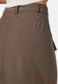 Gonna marrone realizzata in tessuto leggero, con vita piatta e dettagli di cucitura, tasche laterali e vestibilità rilassata.