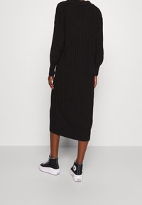 Abito aderente nero a coste con maniche lunghe, lunghezza a metà polpaccio e colletto alto, abbinato a sneakers alte bianche e nere.