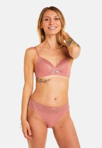 Bralette en dentelle rose clair avec culotte assortie. Le bralette présente un motif texturé et un nœud décoratif. Tissu doux, bretelles réglables.