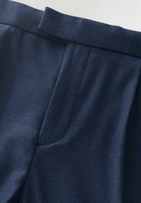 Pantalons ajustés bleu marine au toucher lisse, avec une taille plate, des plis et des poches latérales pour un design structuré.