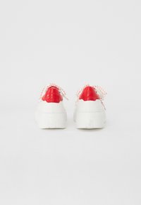 Baskets blanches avec des accents rouges, en matériau texturé, à bout rond et avec des lacets à motifs. Semelle surélevée avec un profil multidirectionnel pour l'adhérence.