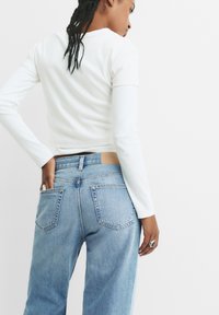 Bela dolgpasovna rebrasta majica v kombinaciji s svetlo modrimi visokimi kavbojkami, ki imajo oznako na zaklopu, dve zadnji žepek in sproščen kroj.