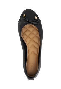 Black ballet flat with a rounded toe, featuring a bow accent and gold hardware. Textured sole is tan with a geometric pattern. Soft material.