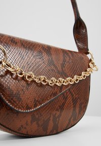 Sac à main marron en simili peau de serpent avec un rabat incurvé et une chaîne décorative dorée sur le devant, doté d'une bandoulière assortie.