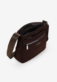 Bolso de hombro de tela marrón con una superficie texturizada, una correa ajustable y un bolsillo frontal con cremallera. El interior es negro con un acabado suave.