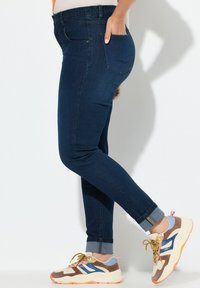 Jean skinny bleu foncé avec poches arrière, taille haute et ourlets retroussés, associés à des chaussures de sport texturées multicolores.