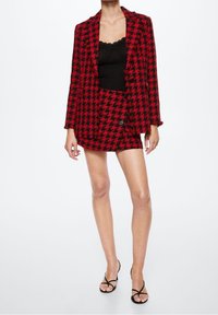 Chaqueta blazer de pata de gallo en rojo y negro combinada con un camisón de encaje negro y una minifalda a juego. Se lleva con sandalias negras de tiras.